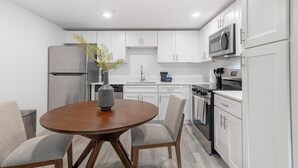 A modern kitchen with white cabinets, stainless steel appliances, and a round wooden table with chairs. - Landing | Spectacular 2BD, Clubhouse, Gym (Kissimmee)