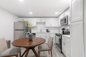 A modern kitchen with white cabinets, stainless steel appliances, and a round wooden table with chairs. - Landing | Stylish 2BD, Pool, Gym (Kissimmee)