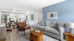 A modern living room with a grey sofa, wooden coffee table, and a dining area with a table and chairs. - Landing | Spectacular 2BD, Clubhouse, Gym (Kissimmee)