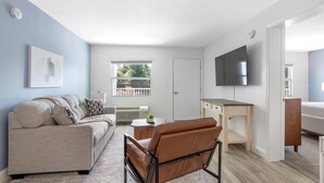 A modern living room with a sofa, a chair, a desk, and a TV mounted on the wall. - Landing | Spectacular 2BD, Clubhouse, Gym (Kissimmee)
