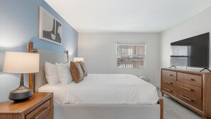 A bedroom with a bed, bedside tables, a dresser, a TV, and a window with blinds. - Landing | Spectacular 2BD, Clubhouse, Gym (Kissimmee)