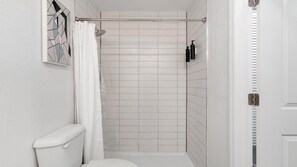 Ein kleines, weißes Badezimmer mit Dusche, Toilette und einem Wandregal mit Toilettenartikeln.