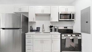 Una cocina compacta con armarios blancos, un refrigerador de acero inoxidable, un microondas, una estufa y un lavamanos.