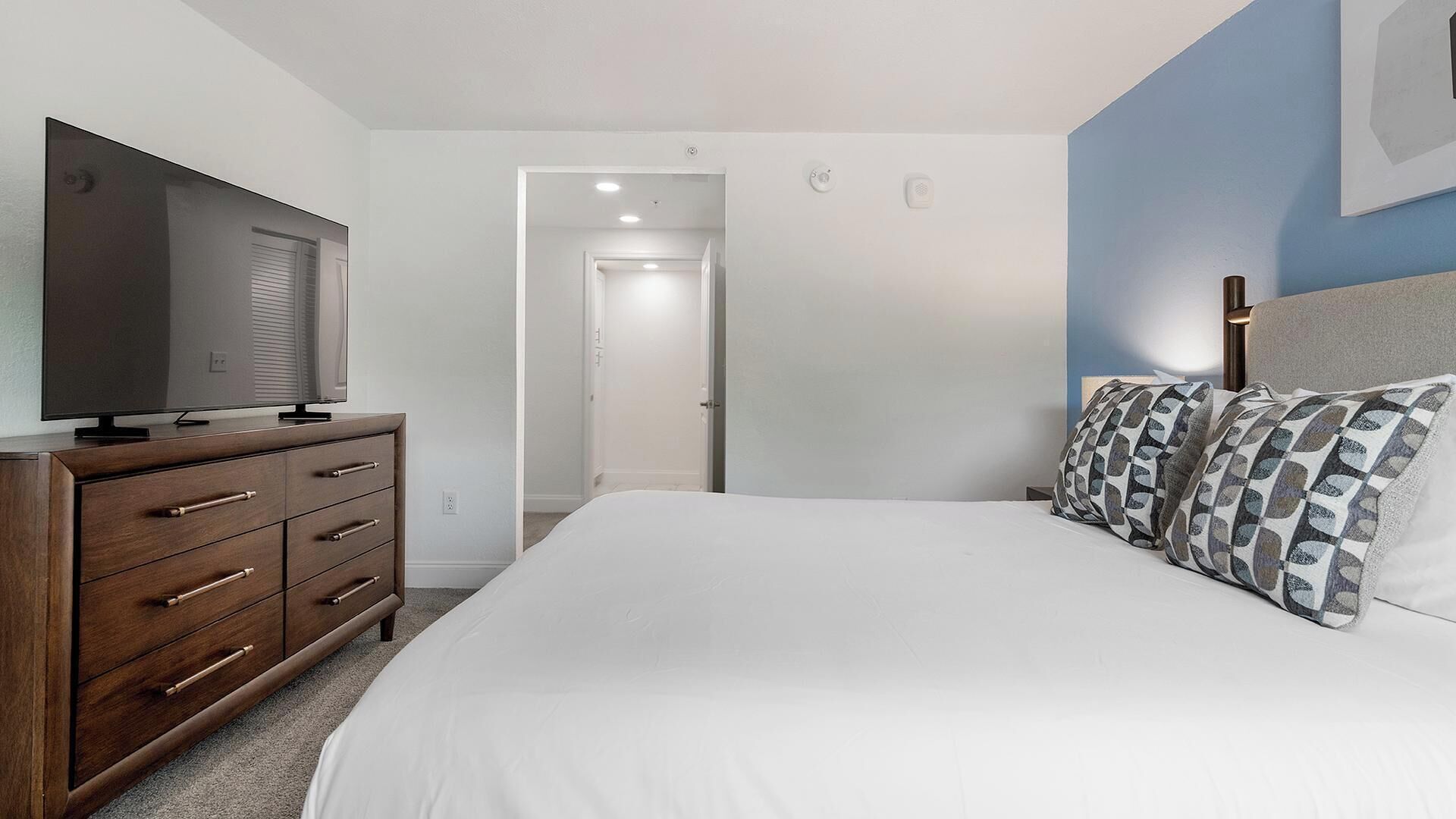 A bedroom with a bed, a TV on a dresser, and a door leading to another room.