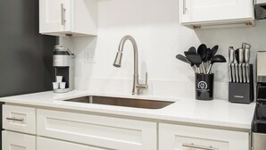 A kitchen with a stainless steel sink, white cabinets, a coffee maker, and a utensil holder. - Landing | Stunning Studio, Pool, Clubhouse (Kissimmee)