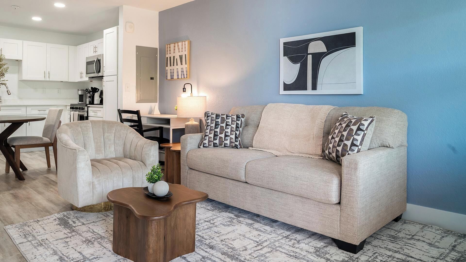 A modern living room with a sofa, armchair, coffee table, and artwork on the wall.