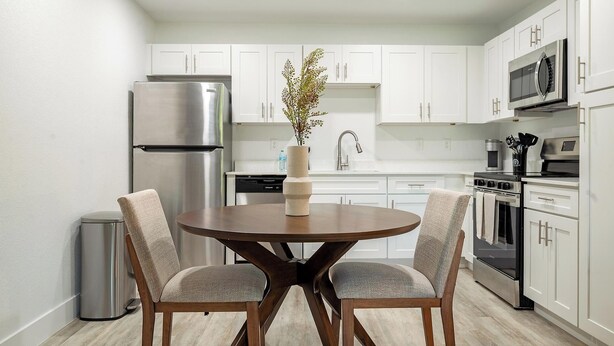 Een moderne keuken met witte kastjes, roestvrijstalen apparatuur en een ronde houten tafel met twee stoelen.