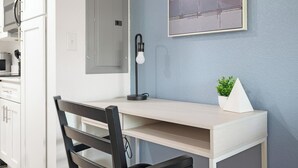 Eine moderne Küche mit weißen Schränken, einem schwarzen Stuhl, einem Schreibtisch mit Lampe und einer kleinen Pflanze an der Wand.