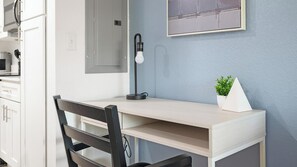 A modern kitchen with white cabinets, a black chair, a desk with a lamp, and a small plant on the wall. - Landing | Chic 1BD, Gym, Clubhouse (Kissimmee)