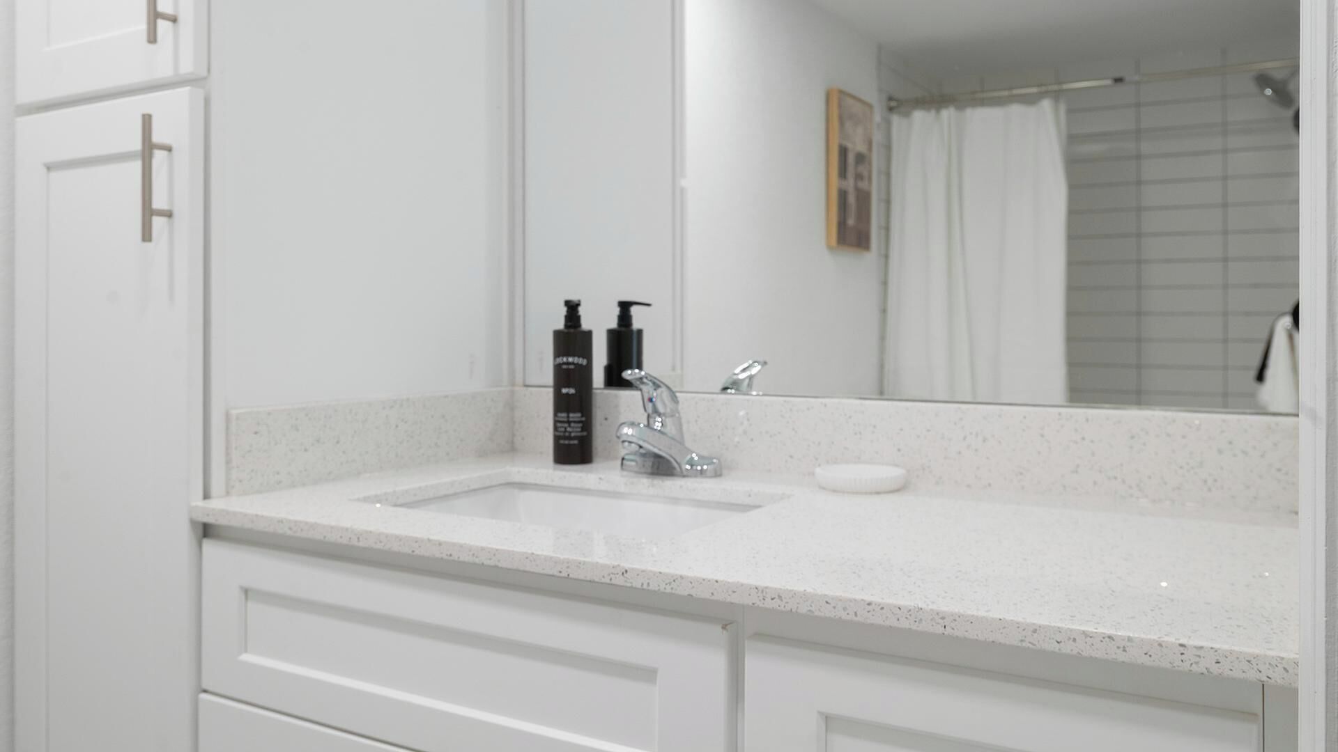 A bathroom with a white sink, a mirror, and two bottles of shampoo.
