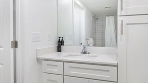 A bathroom with a white sink, a mirror, and a shower curtain. - Landing | Beautiful 1BD, Gym, Pool (Kissimmee)