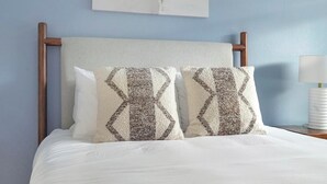 A bed with white bedding, two patterned pillows, a wooden headboard, and a nightstand with a lamp. - Landing | Amazing 1BD, Pool, Gym (Kissimmee)