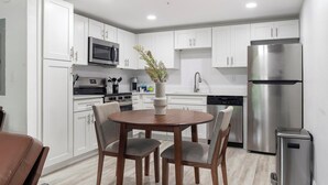 A modern kitchen with white cabinets, stainless steel appliances, a dining table with chairs, and a vase with flowers. - Landing | Amazing 1BD, Pool, Gym (Kissimmee)