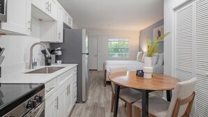Eine kompakte Küche mit Spüle, Herd und Schränken, ein Essbereich mit Tisch und Stühlen sowie ein Schlafzimmer mit Bett und Fenster.