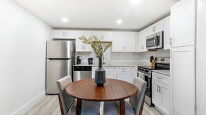 A modern kitchen with white cabinets, stainless steel appliances, and a round wooden table with chairs. - Landing | Stylish 1BD, Clubhouse, Gym (Kissimmee)