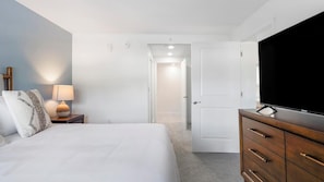 A hotel room with a bed, a TV, a dresser, and a nightstand with a lamp. - Landing | Stylish 1BD, Clubhouse, Gym (Kissimmee)