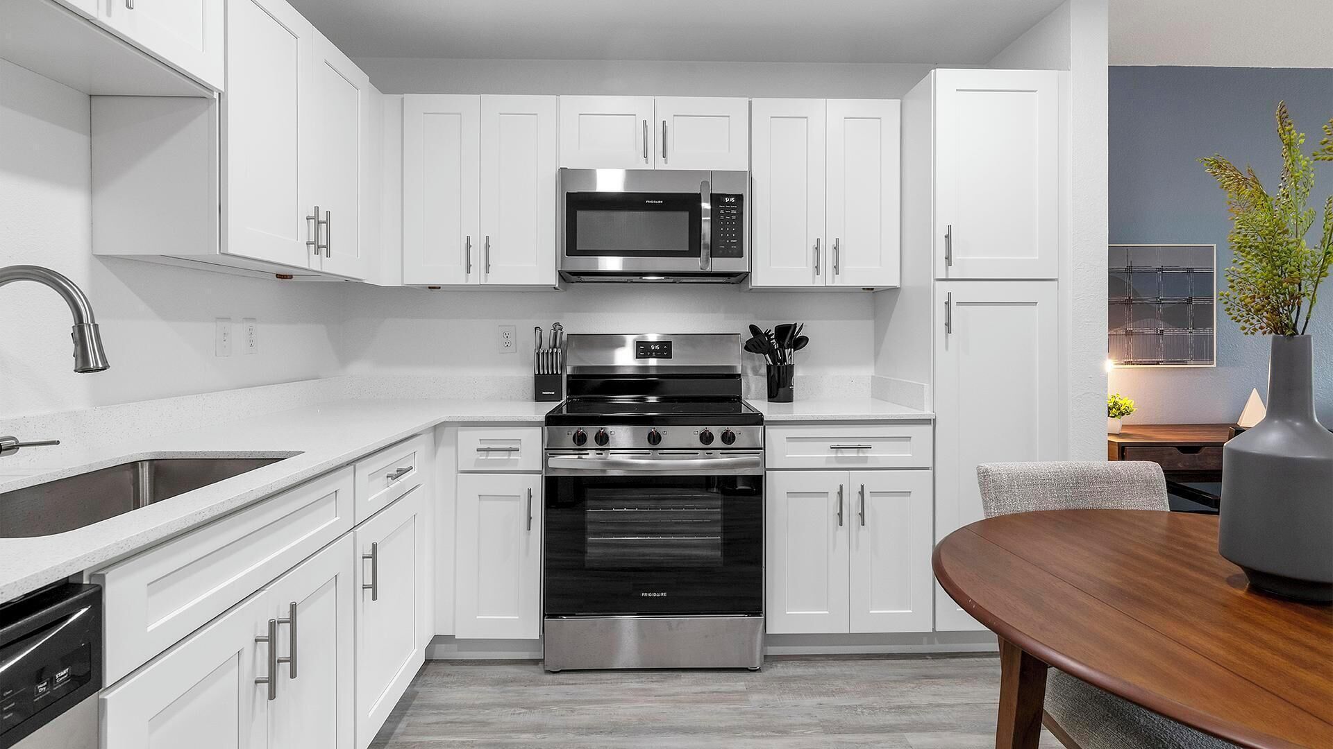 Una cocina moderna con armarios blancos, electrodomésticos de acero inoxidable y una mesa de comedor de madera.