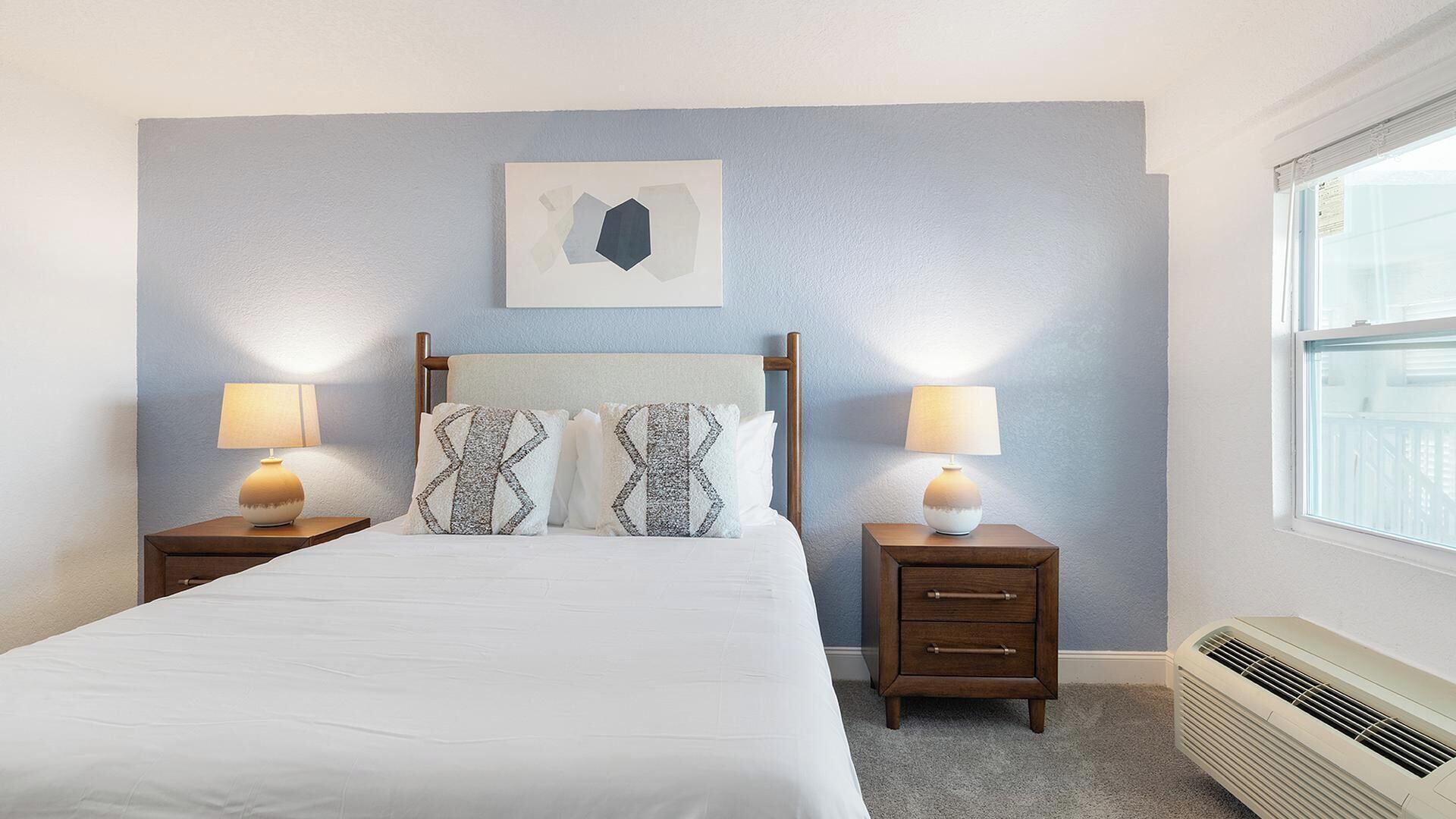 Una camera da letto con un letto, due comodini con lampade, un'opera d'arte appesa al muro e una finestra.