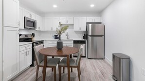 Une cuisine moderne avec des meubles blancs, un réfrigérateur en acier inoxydable, un four à micro-ondes et une table à manger avec des chaises.