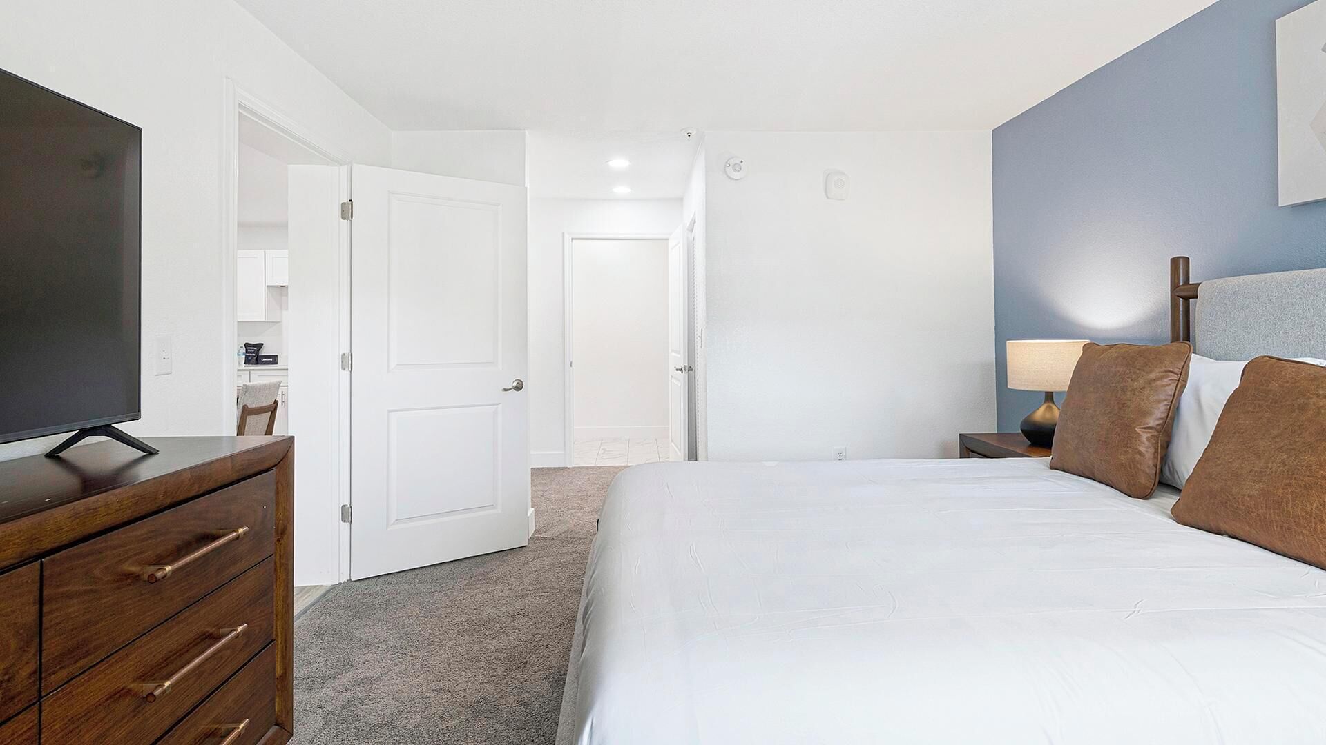 A hotel room with a bed, a TV, a dresser, and a nightstand with a lamp.