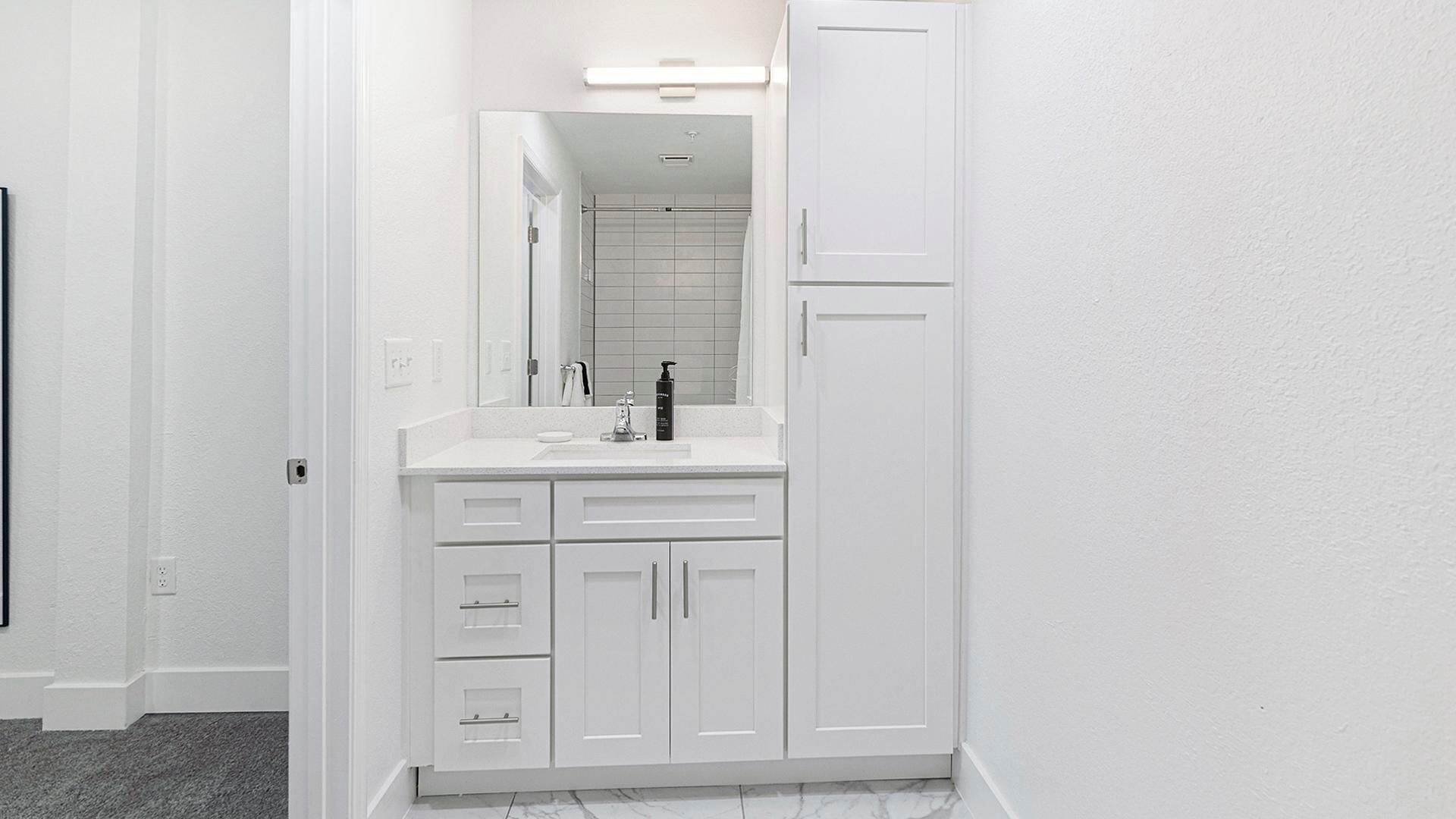 Une salle de bain avec des meubles blancs, un miroir, un lavabo et des toilettes.
