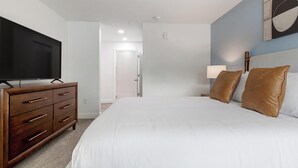 A hotel room with a bed, a dresser, a television, and a nightstand with a lamp. - Landing | Incredible 1BD, Pool, Gym (Kissimmee)