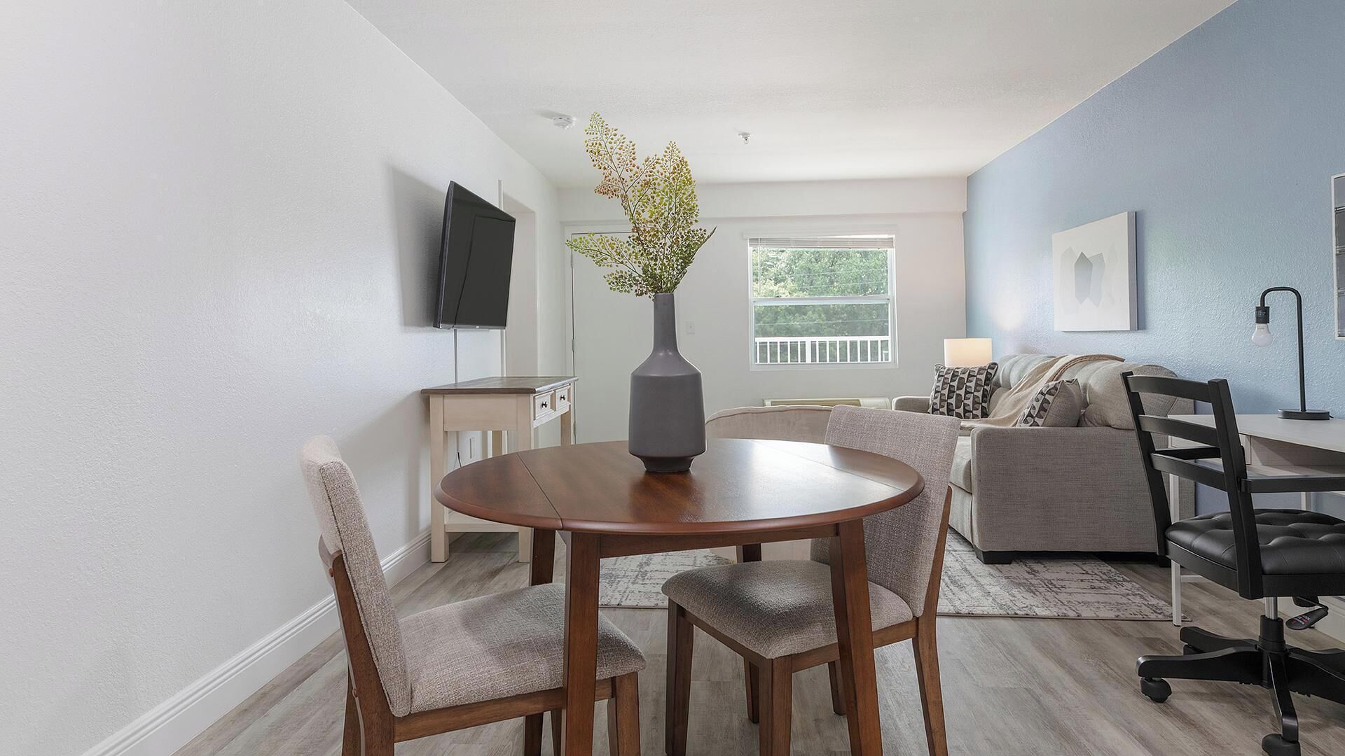 Ein modernes Wohnzimmer mit Esstisch, Stühlen, einer Couch, einem Fernseher und einer Vase mit Blumen.