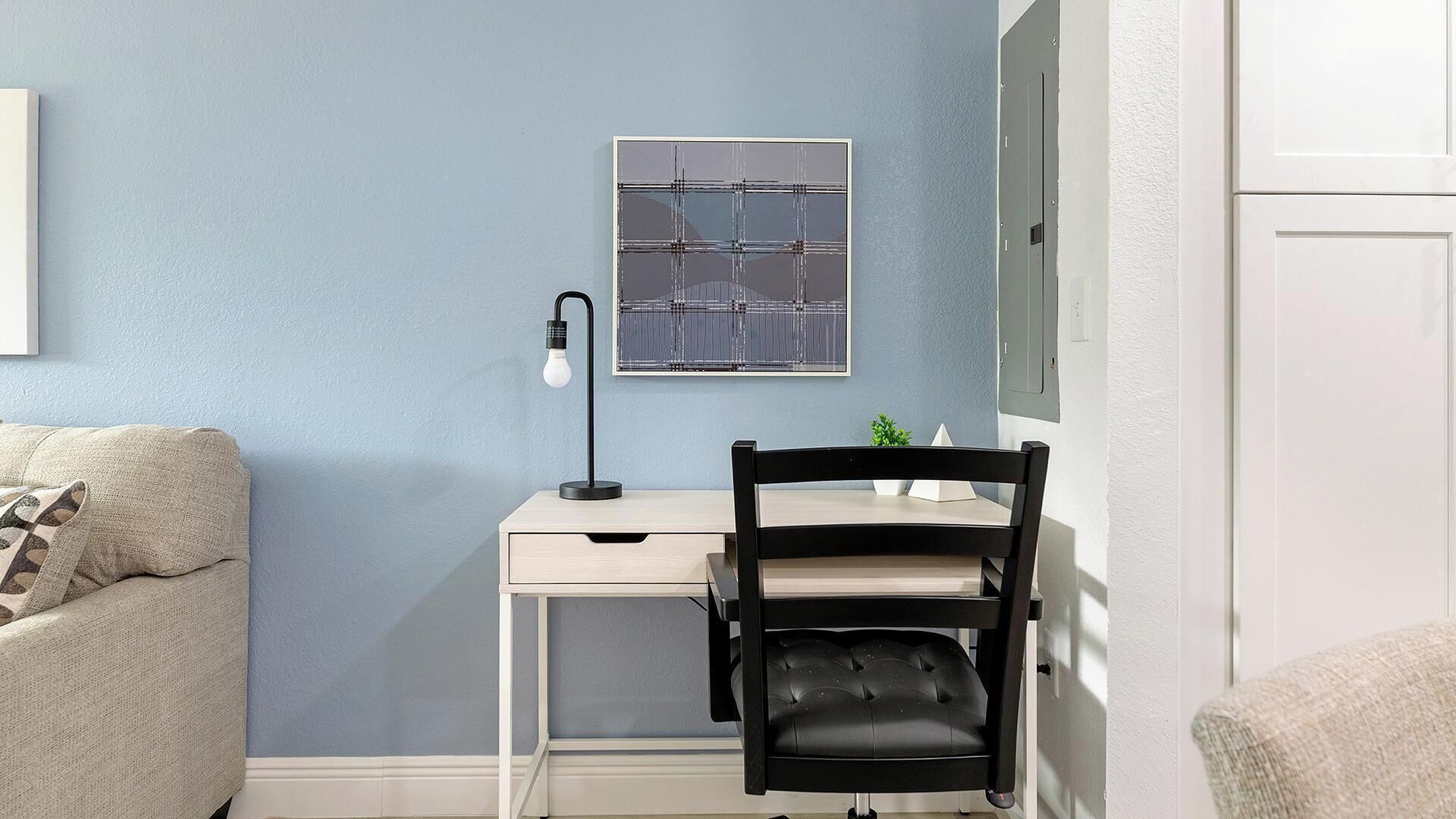 Quarto com escrivaninha, cadeira e luminária na parede.