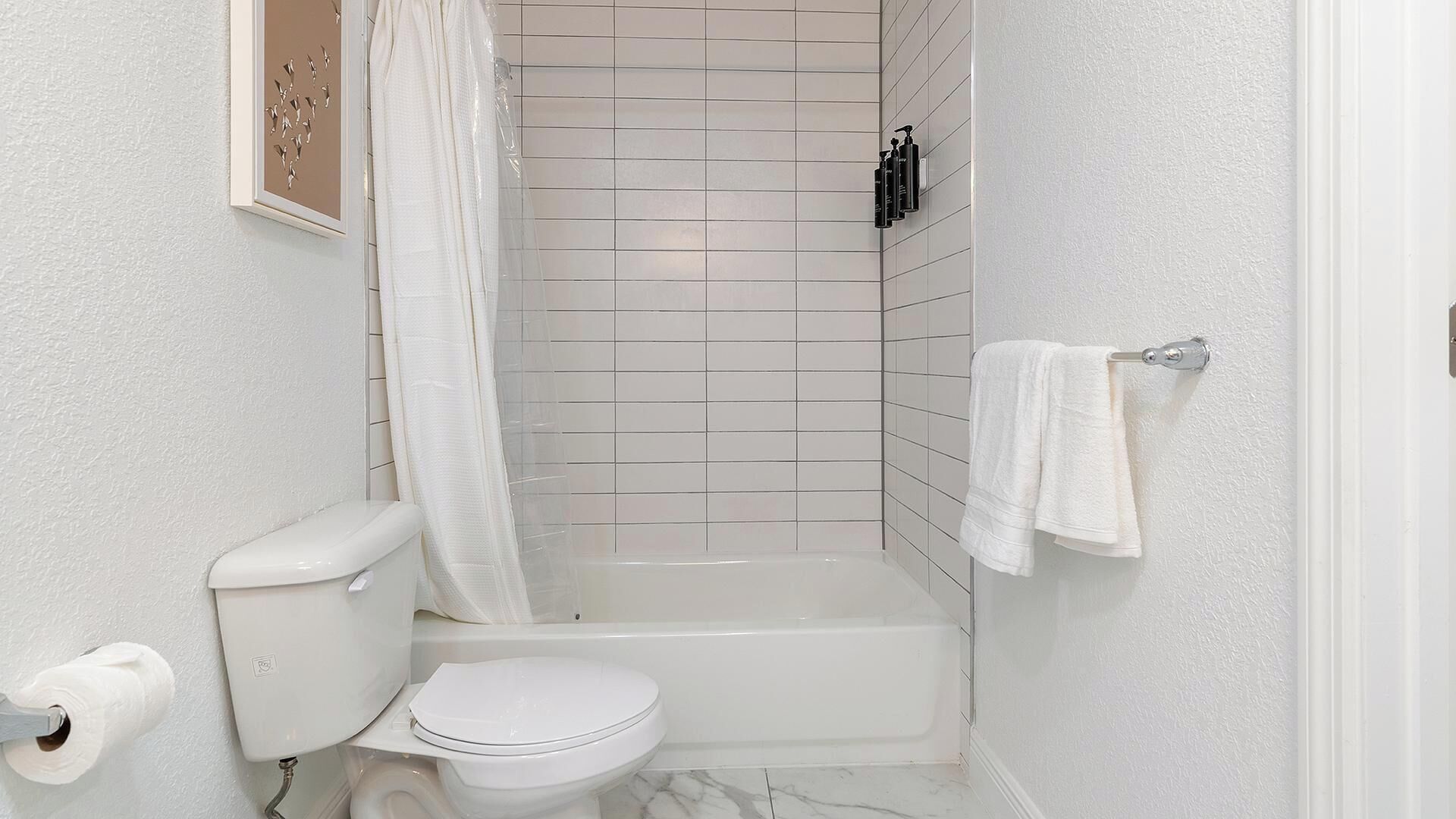 Une salle de bain équipée de toilettes, d’une baignoire, d’un rideau de douche et d’un porte-serviettes.