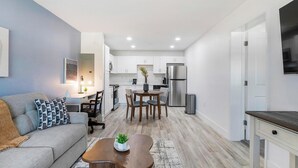 A compact living space with a sofa, coffee table, dining table, and kitchen area including a refrigerator and cabinets. - Landing | Stunning 1BD, Clubhouse, Pool (Kissimmee)