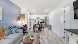 A compact living space with a sofa, coffee table, dining table, and kitchen area including a refrigerator and cabinets. - Landing | Modern 1BD, Clubhouse, Pool (Kissimmee)