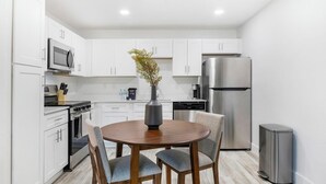 A modern kitchen with white cabinets, stainless steel appliances, a round wooden table, and two chairs. - Landing | Stunning 1BD, Clubhouse, Pool (Kissimmee)