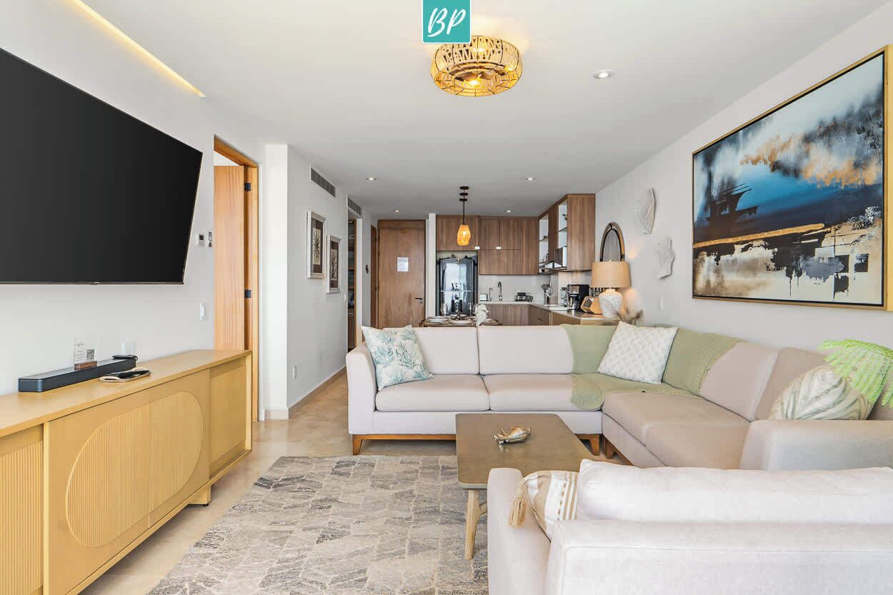 A modern living room with a sofa, coffee table, TV, and a kitchen in the background.