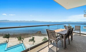Un balcón con vista al mar, una piscina y una mesa con sillas.