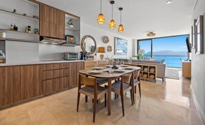 Una cocina moderna con armarios de madera, un comedor con una mesa redonda dispuesta para cuatro personas y un amplio ventanal con vistas al agua.