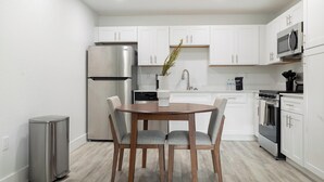 Une cuisine moderne avec des meubles blancs, des appareils en acier inoxydable, une table ronde en bois et deux chaises.