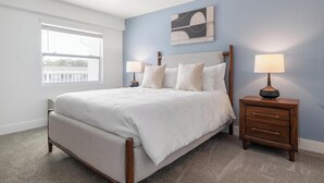 Une chambre à coucher comprenant un lit, deux tables de chevet, une fenêtre et une œuvre d’art accrochée au mur.