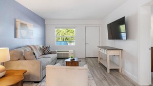 A living room with a sofa, coffee table, TV, and a window with a view. - Landing | Modern 1BD, Gym, Clubhouse (Kissimmee)