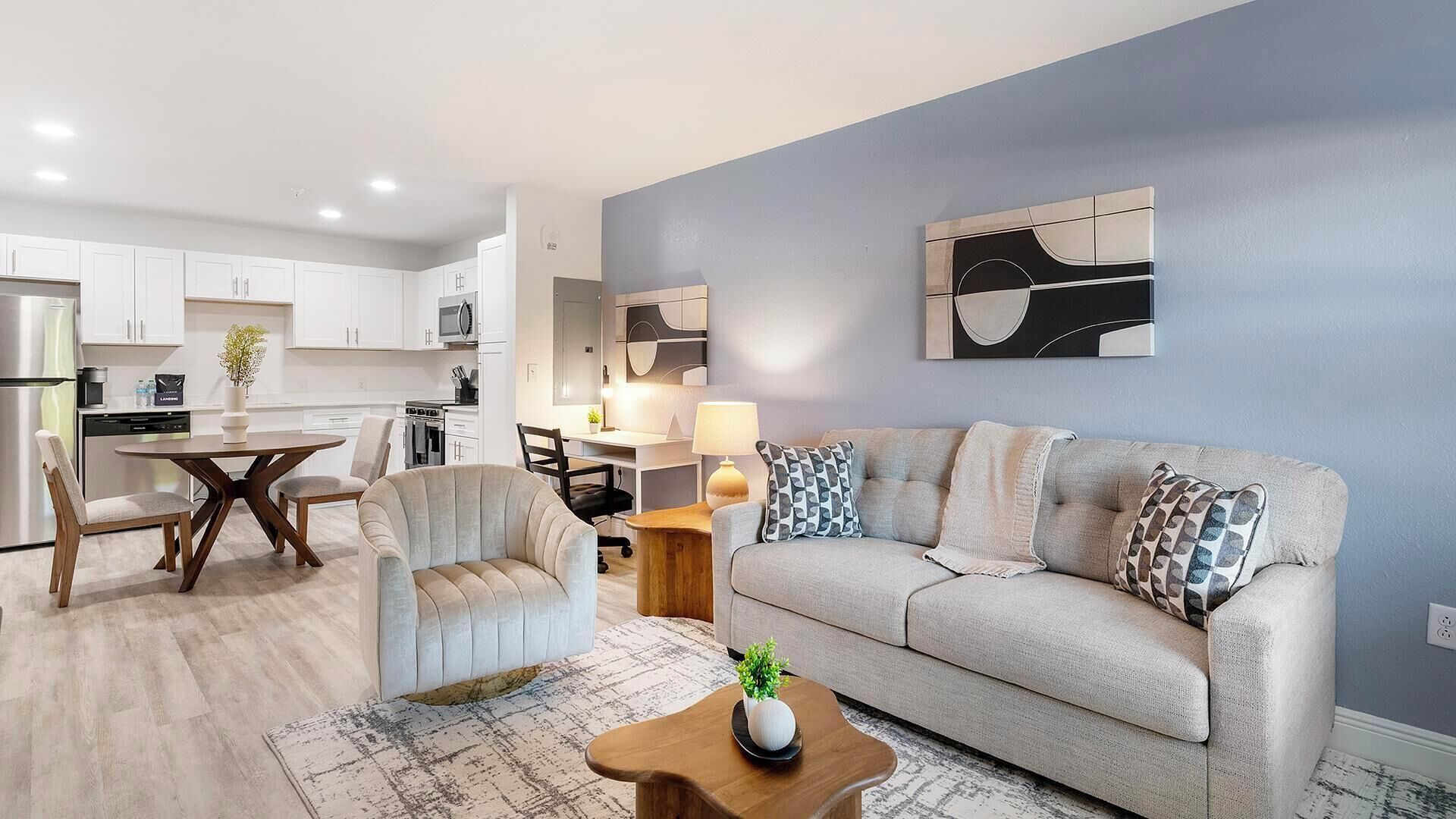A modern living room with a sofa, armchair, coffee table, and a dining area with a table and chairs.