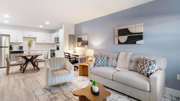 A modern living room with a sofa, armchair, coffee table, and a dining area with a table and chairs. - Landing | Modern 1BD, Gym, Clubhouse (Kissimmee)