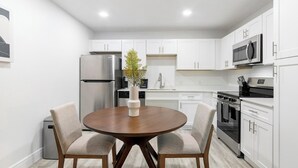 A modern kitchen with white cabinets, stainless steel appliances, a round wooden table, and two chairs. - Landing | Modern 1BD, Gym, Clubhouse (Kissimmee)
