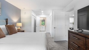 A hotel room with a bed, bedside table, lamp, TV, wardrobe, and a bathroom visible through an open door. - Landing | Modern 1BD, Gym, Clubhouse (Kissimmee)