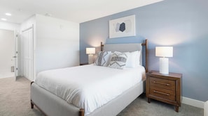 A bedroom with a bed, two bedside tables, a nightstand, a door, and a wall-mounted artwork. - Landing | Stylish 1BD, Clubhouse, Pool (Kissimmee)