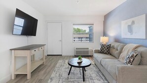Ett modernt vardagsrum med en platt-TV, en soffa, ett soffbord och ett fönster med utsikt över byggnader.