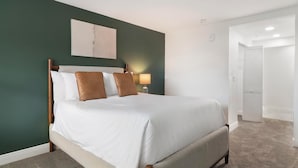 Ein ordentlich bezogenes Bett mit weißen Laken und braunen Kissen, eine Nachttischlampe und ein an der Wand hängendes Kunstwerk darüber.