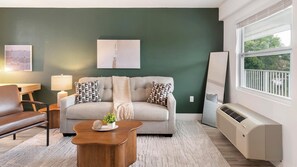 Ein Wohnzimmer mit einer Couch, einem Couchtisch, einer Lampe, einem Heizkörper und einem Fenster.