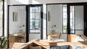 Un interior moderno con un ventanal grande, una mesa redonda y una zona de estar con sofá y sillones.