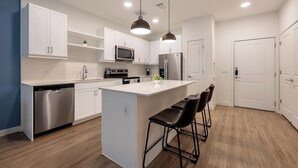 Una cocina moderna con armarios blancos, electrodomésticos de acero inoxidable y una isla central con taburetes de bar.