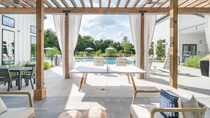 Un espacio de estar al aire libre cubierto, con vista a la piscina, una pérgola de madera y muebles de exterior modernos.