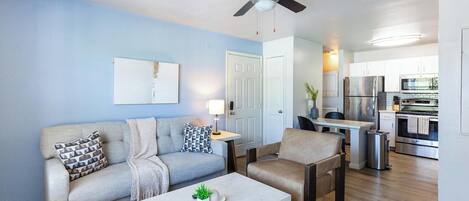 A living room with a sofa, armchair, coffee table, and a ceiling fan.